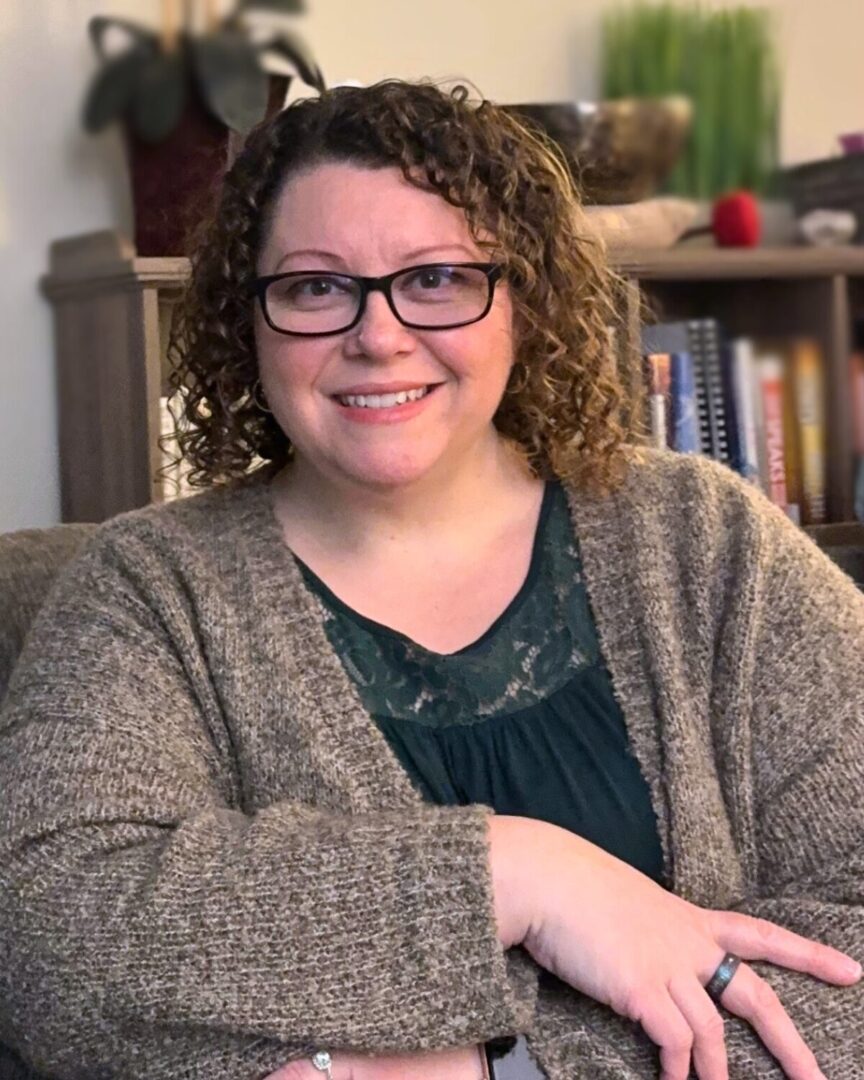 Samantha Schalk seated in an office setting, smiling, with a blurred bookshelf in the background.